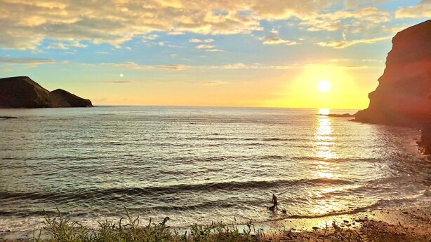 Ein Sonnenuntergang über ruhigem Meer, flankiert von Klippen.