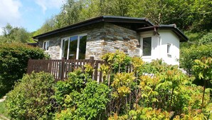 Ein Steinhhaus mit einer Holzterrasse und üppiger Bepflanzung.