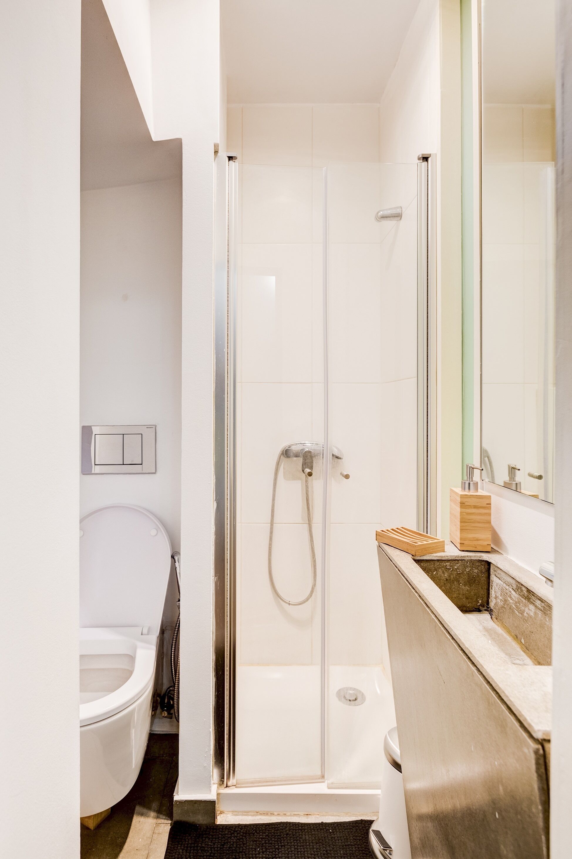 Une salle de bain moderne avec une douche à parois de verre, des toilettes blanches et un meuble-lavabo en bois doté d’un miroir.