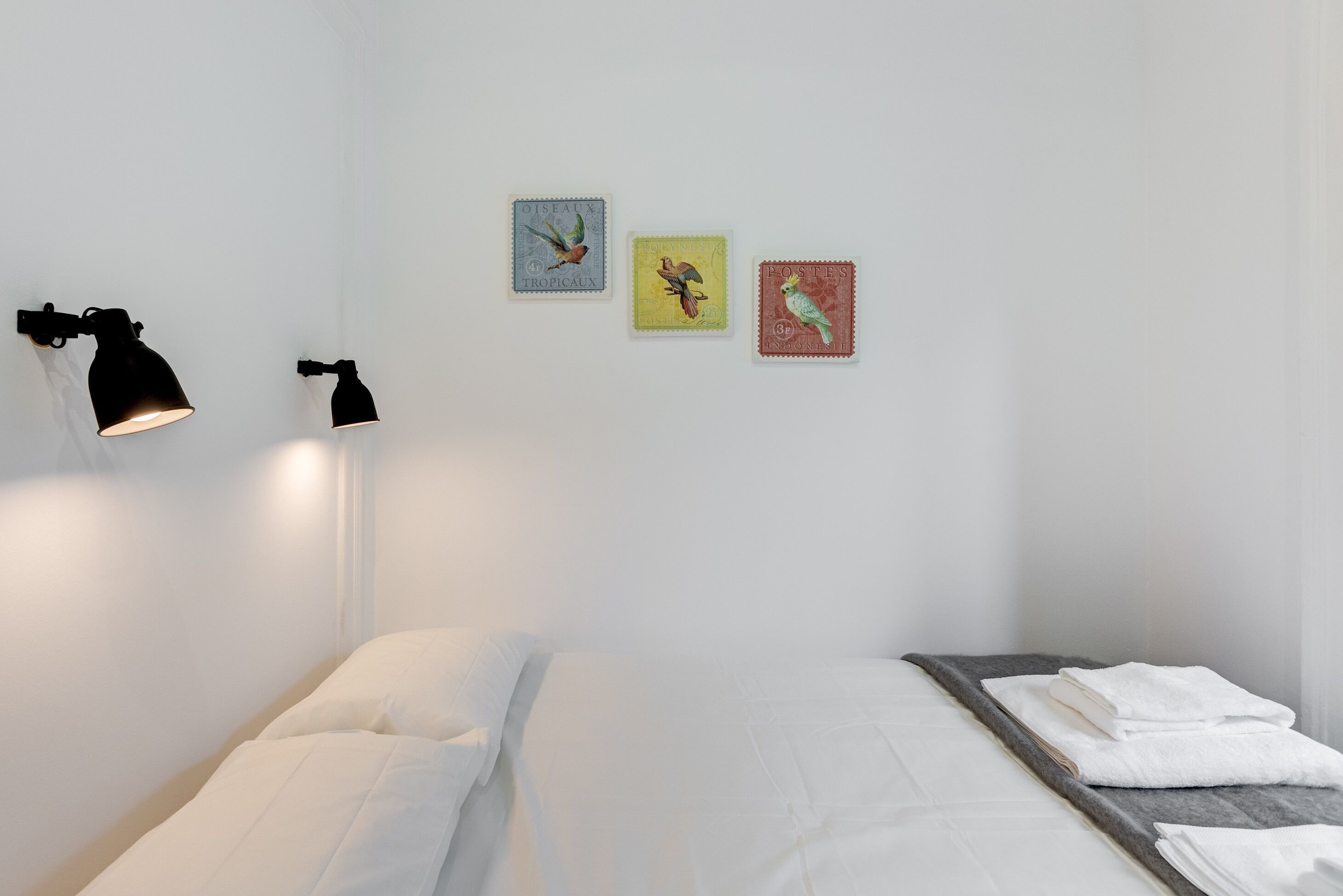 Une chambre à coucher au style minimaliste, avec un lit, une table de chevet et des lampes fixées au mur.