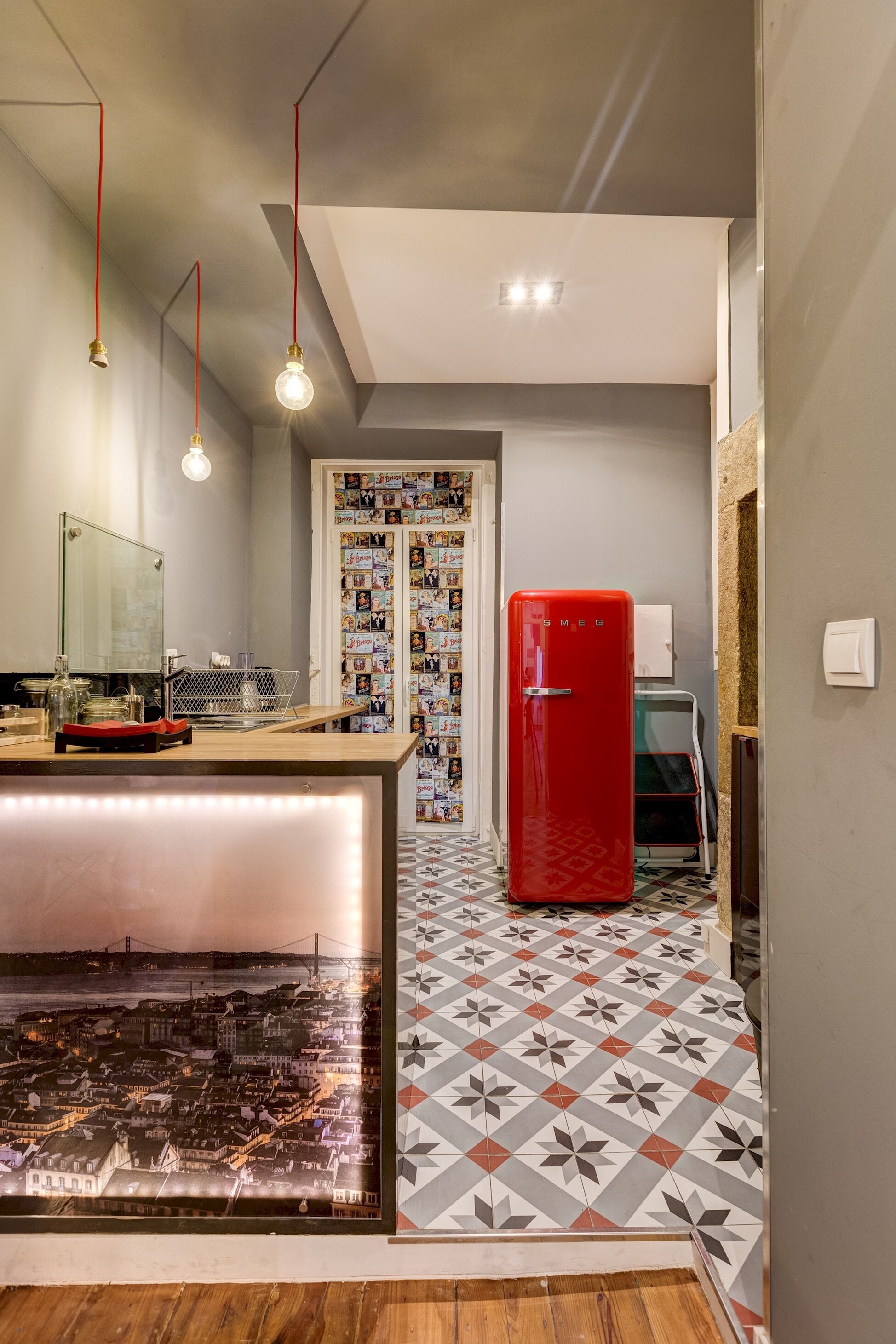 A modern kitchen with a central island, a red refrigerator, and a tiled backsplash.