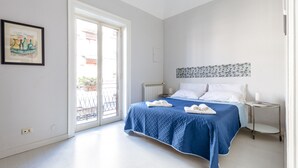 A bedroom with a bed, a bedside table, a radiator, a window, and a door.