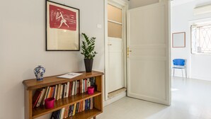 A hallway with a bookshelf, a framed picture, a potted plant, and a door leading to another room.