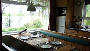 A kitchen with a dining area, a microwave, a refrigerator, and a window with a view of greenery. - Cottage 9 -  a cottages  that sleeps 6 guests  in 0 bedrooms (Irvinestown)