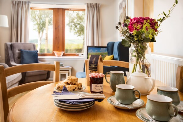A dining table with a plate of scones, a jar of jam, and a vase of flowers.