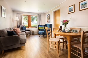 A cozy living room with a sofa, a dining table with chairs, a TV, and a window with curtains.