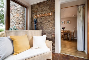 A room with a stone wall, wicker sofa, and a dining area with a table and chairs.