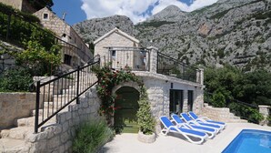 Un edificio de piedra con piscina y sillas de descanso, rodeado de montañas.