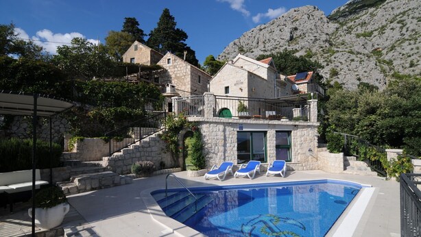 Un edificio de piedra con piscina y sillas de descanso.