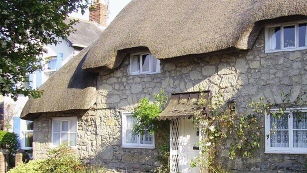 Une maison en pierre avec des toits de chaume et des cadres de fenêtres blancs.