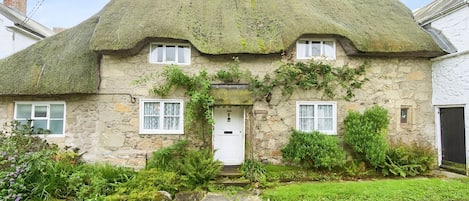 A stone house with a thatched roof, ivy-covered walls, and a white door.