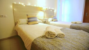 A hotel room with two beds, each with a headboard, a bedside table with a lamp, and a window with curtains. - Spacious apartment in the Center of Palma, Ideal for Families. (Palma)