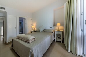 Een slaapkamer met een bed, twee nachtkastjes met lampen, een deur en een gordijn.