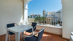 A balcony with a white table and chairs, a tiled floor, and a view of buildings in the distance. - Las Dunas - Punta del Moral Beach PLHD115P113 (Punta del Moral)