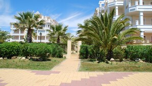 A gated entrance to a residential complex with palm trees and a paved walkway. - Las Dunas - Punta del Moral Beach PLHD115P113 (Punta del Moral)