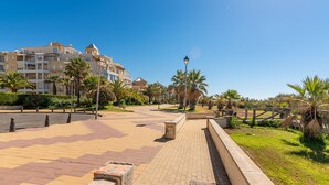 A paved promenade with palm trees, a lamp post, and a building with balconies in the background. - Las Dunas - Punta del Moral Beach PLHD115P113 (Punta del Moral)