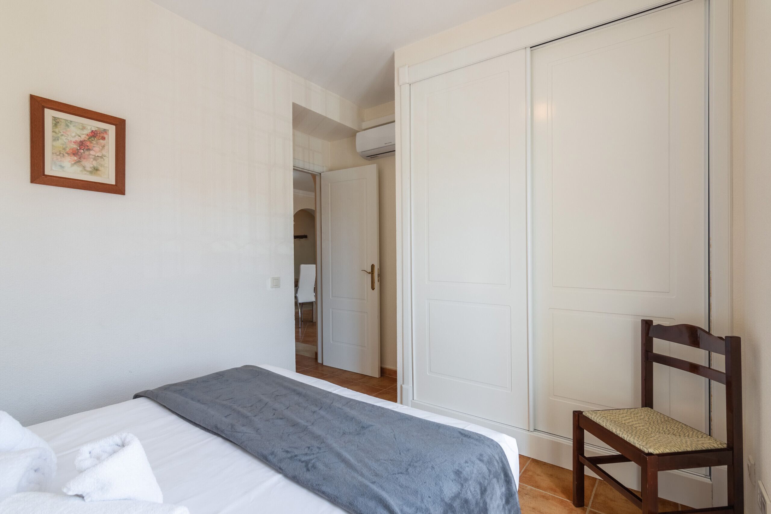 Quarto com cama, cadeira, guarda-roupa e porta que dá para outro espaço.