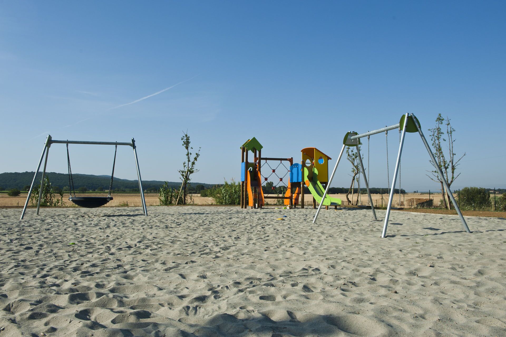 Un’area giochi con altalene e strutture da arrampicata su una spiaggia sabbiosa.