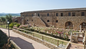 A stone building with arched windows and a tiled roof, surrounded by a stone wall and a paved walkway.