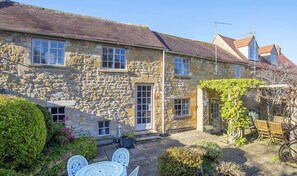 A stone building with a tiled roof, a front door, and a small garden with a table and chairs. - Box Cottage - sleeps 4 guests in 2 bedrooms (Broadway)