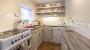 Une cuisine compacte avec des meubles blancs, un lave-vaisselle Bosch, une cuisinière et un évier.