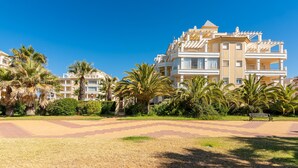 A hotel with multiple balconies, palm trees, and a paved walkway. - Las Dunas - Punta del Moral Beach PLHD141P160 (Punta del Moral)