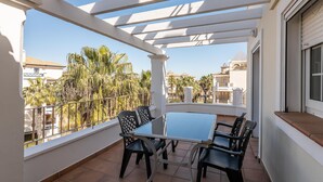 A balcony with a glass table and chairs, white railings, and a view of palm trees and buildings. - Las Dunas - Punta del Moral Beach PLHD141P160 (Punta del Moral)