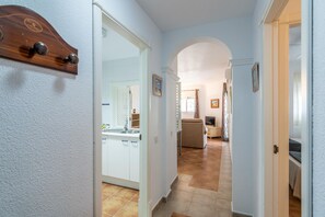 A hallway leading to a kitchen with white cabinets, a sink, and a dining area with a sofa and table.
