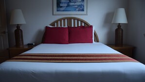 A neatly made bed with a wooden headboard, two bedside lamps, and a painting on the wall. - Schooner Landing (Newport)