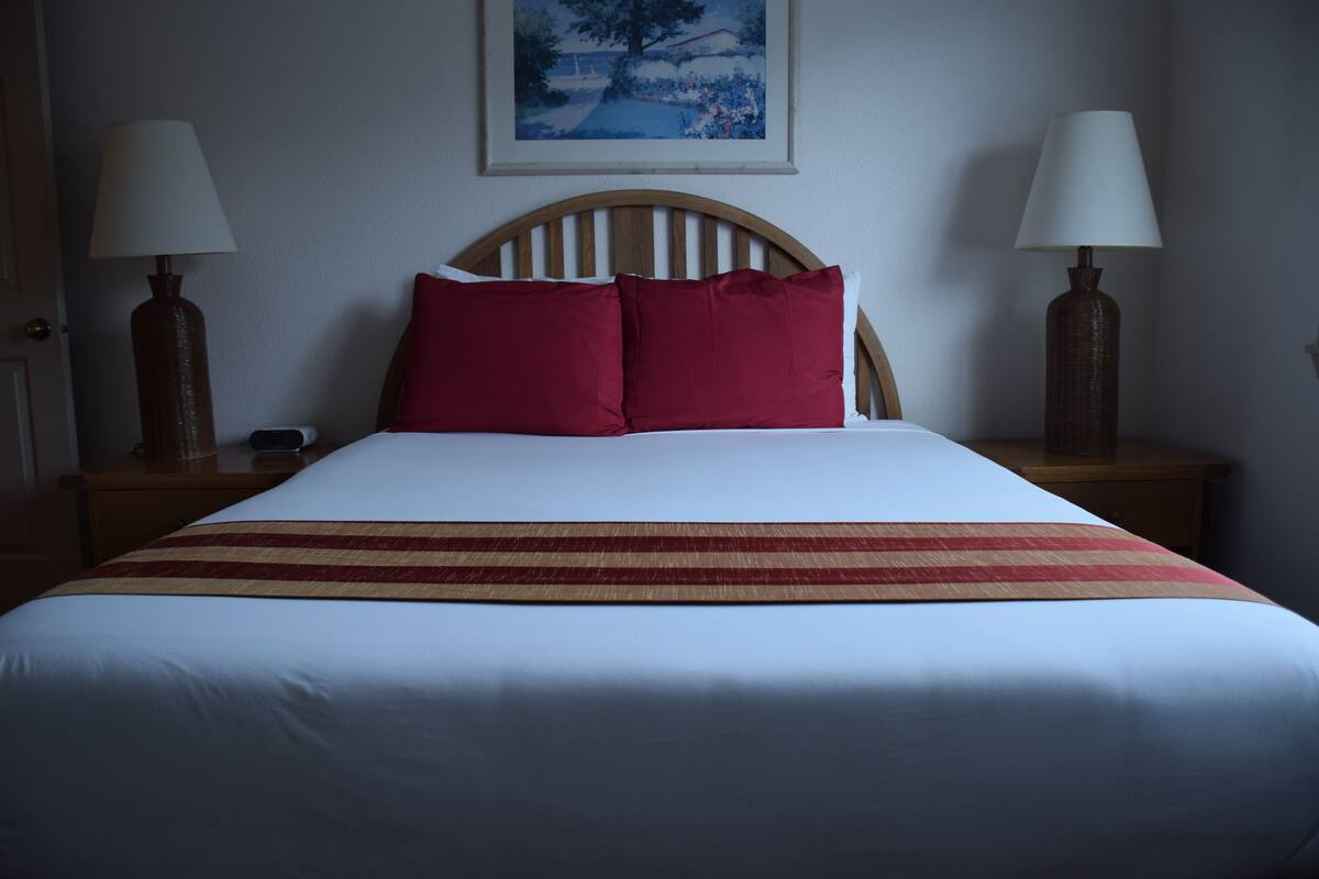 A neatly made bed with a wooden headboard, two bedside lamps, and a painting on the wall.