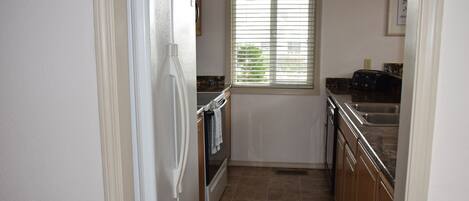 A kitchen with a refrigerator, oven, sink, and window.