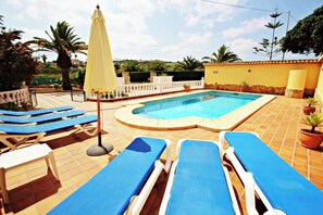 Une piscine avec des chaises longues bleues et un parasol jaune.