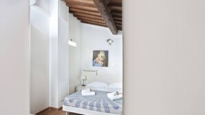 Une chambre à coucher comprenant un lit, une table de chevet, un radiateur fixé au mur et un plafond avec des poutres apparentes.