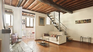 Un salon comprenant un canapé, une table basse, un téléviseur, un escalier et des œuvres d’art accrochées au mur.