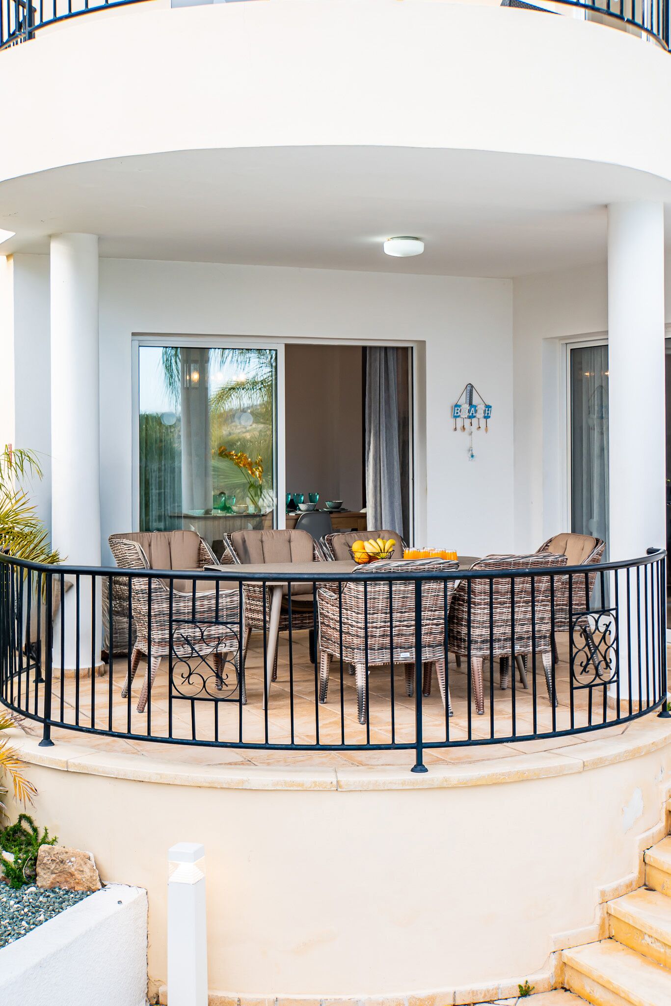 Een balkon met rieten meubilair, een eettafel en uitzicht op de omgeving.