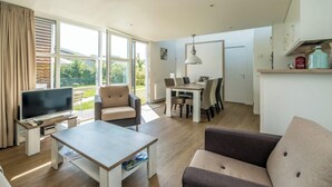 Een ruime woonkamer met een televisie, bank, eettafel en stoelen.