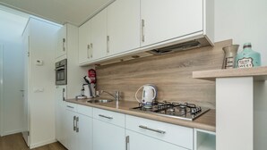 Een moderne keuken met witte kastjes, een gasfornuis, een spoelbak en een houten achterwand.