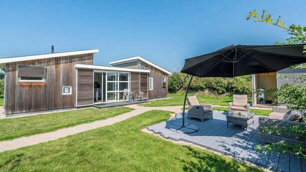 Een modern huis met een patio, tuinmeubilair en een grote parasol.