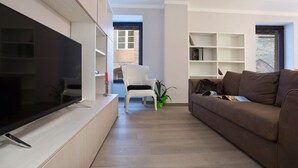 A modern living room with a flat-screen TV, a brown sofa, a white chair, and a bookshelf. - THE TOLOMEI - apartment in the heart of the main street (Siena)