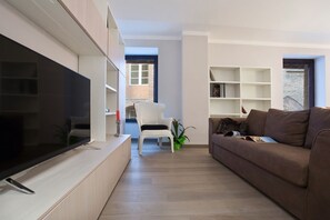Un salon moderne avec un téléviseur à écran plat, un canapé marron, un fauteuil blanc et une bibliothèque.