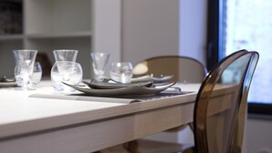 A dining table set with clear glassware and plates, a wooden chair, and a window in the background. - THE TOLOMEI - apartment in the heart of the main street (Siena)