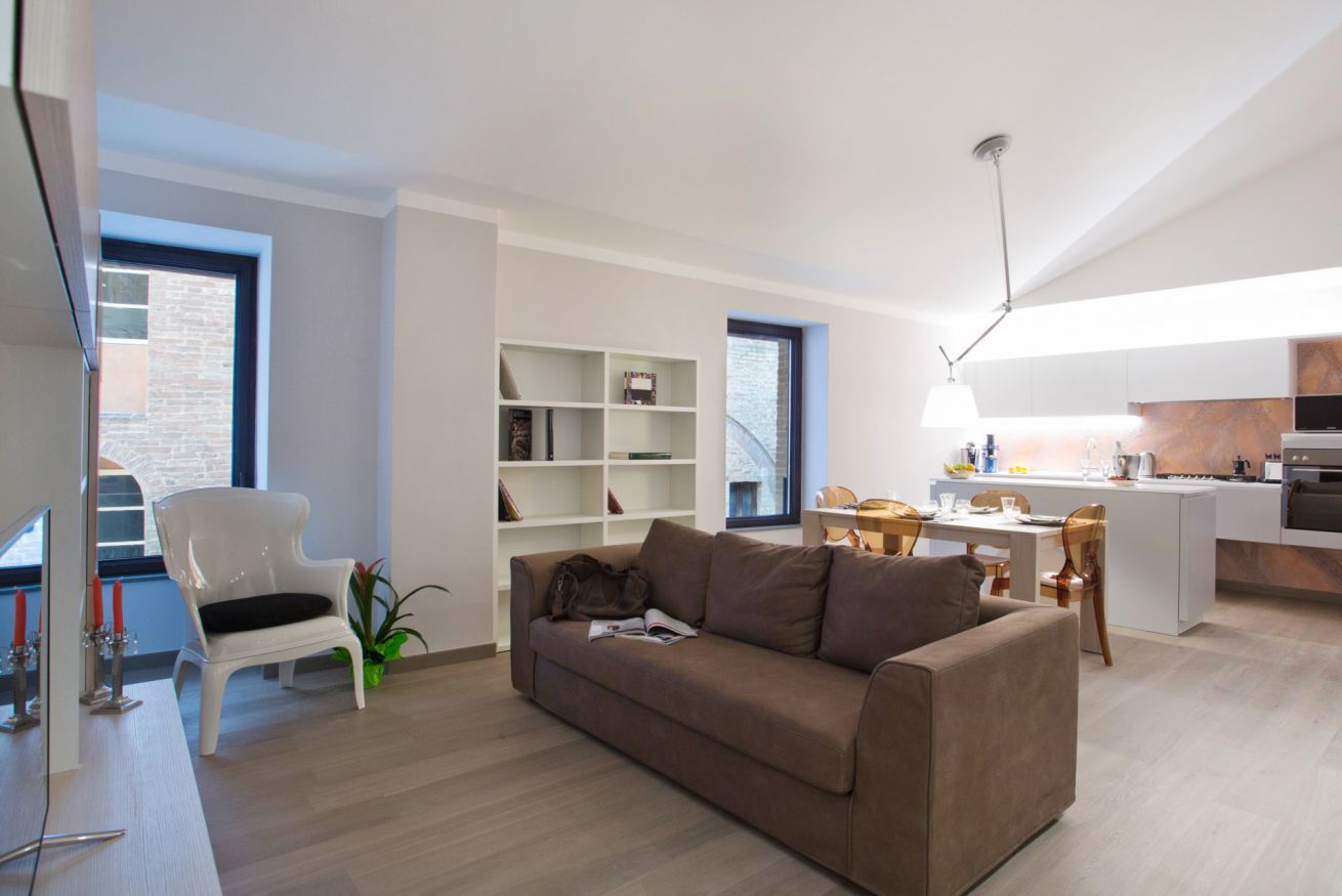 Een moderne woonkamer met een bruine bank, witte planken en een eethoek, met een keuken op de achtergrond.