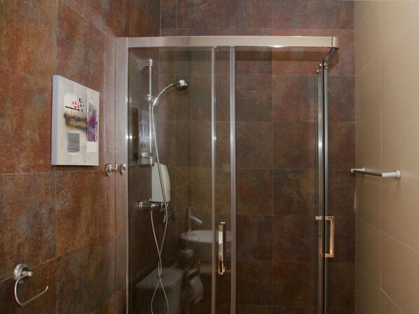 Une cabine de douche fermée par des parois en verre, dotée d’un pommeau de douche à main et d’un robinet fixé au mur.