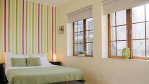 Ein Schlafzimmer mit Bett, Nachttisch, Bank, Fenster mit Blick und einer gestreiften Wand.