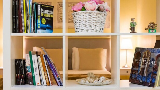 A bookshelf with books, a wicker basket with flowers, a plate with seashells, and a book titled "A Walk in Portugal".