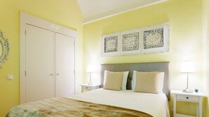 A bedroom with a bed, two bedside tables, a nightstand, a wardrobe, and decorative wall art.