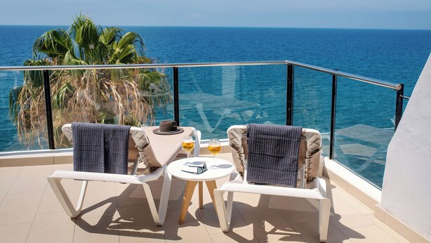 A balcony with two white lounge chairs, a small round table, and a view of the ocean. - ESTELAI by Buenavilla | Apartment with breathtaking front line Ocean views (Tías)
