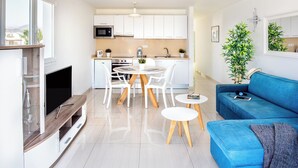 A modern living room with a blue sofa, a TV, and a dining area with a table and chairs. - ESTELAI by Buenavilla | Apartment with breathtaking front line Ocean views (Tías)