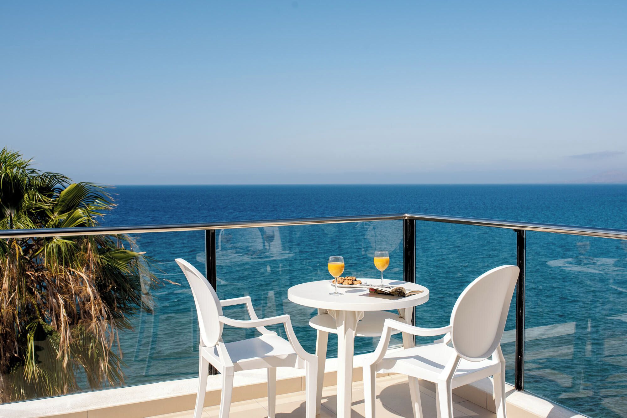 A balcony with a table and chairs overlooking the sea.