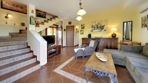 A spacious living area with a staircase, a television, wicker furniture, and artwork on the walls. - Wonderful private villa for 8 people with private pool, WIFI, A/C and TV (Marina Di Ragusa)